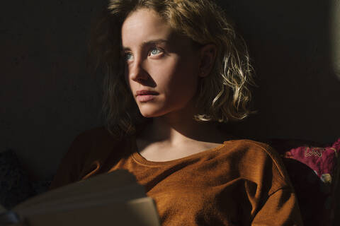 Portrait of pensive student with book looking at distance stock photo