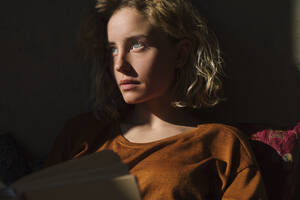 Porträt eines nachdenklichen Studenten mit Buch, der in die Ferne schaut - GCF00259