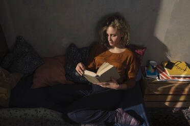Blonde Studentin sitzt auf dem Bett und liest ein Buch - GCF00260