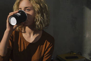 Blond young woman drinking coffee to go at home - GCF00269