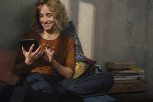 Porträt einer lächelnden jungen Frau, die auf dem Bett sitzt und ein E-Book liest - GCF00272