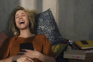 Porträt einer lachenden jungen Frau auf dem Bett liegend mit E-Book-Reader - GCF00279