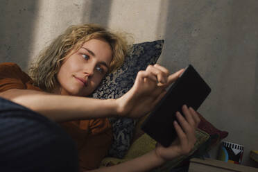 Porträt einer jungen Frau, die auf dem Bett liegt und ein E-Book liest - GCF00280