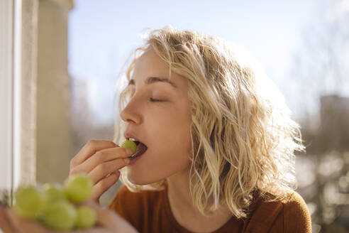 Porträt einer blonden jungen Frau, die grüne Weintrauben isst - GCF00281