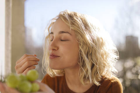 Porträt einer blonden jungen Frau, die grüne Weintrauben isst, lizenzfreies Stockfoto