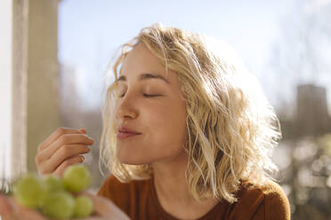 Porträt einer blonden jungen Frau, die grüne Weintrauben isst - GCF00282