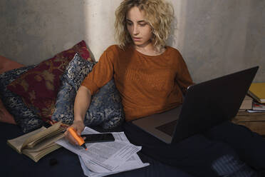 Porträt einer blonden Studentin, die mit einem Laptop auf dem Bett sitzt und arbeitet - GCF00286