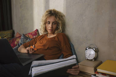Porträt einer blonden Studentin auf dem Bett, die an einem Laptop arbeitet - GCF00289