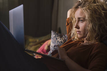 Porträt einer blonden jungen Frau, die auf dem Bett liegt und einen Laptop benutzt - GCF00293