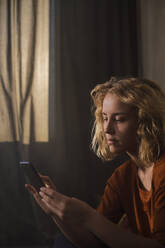 Porträt einer blonden jungen Frau, die ein Mobiltelefon benutzt - GCF00296
