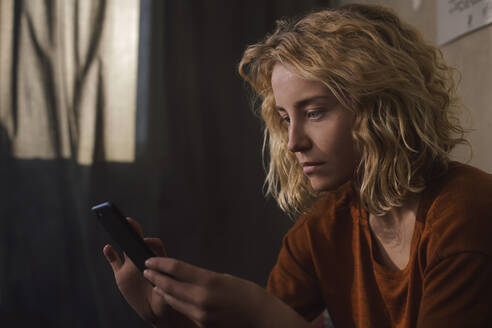 Porträt einer blonden jungen Frau, die ein Mobiltelefon benutzt - GCF00297