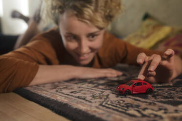 Junge Frau liegt auf einem Teppich und spielt mit einem roten Spielzeugauto - GCF00308