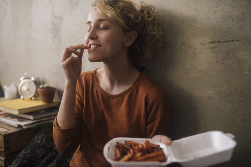 Porträt einer jungen Frau, die zu Hause Pommes frites isst - GCF00310