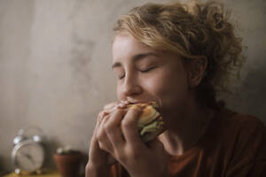 Porträt einer jungen Frau, die einen Hamburger isst - GCF00311