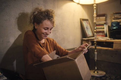 Smiling young woman unpacking parcel at home - GCF00312