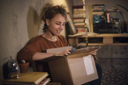 Smiling young woman unpacking parcel at home - GCF00313