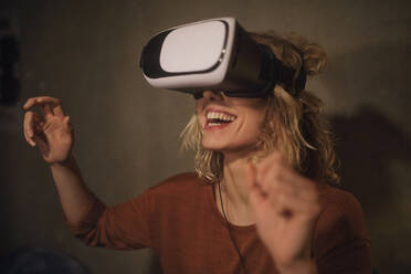 Laughing young woman using Virtual Reality Glasses at home - GCF00320