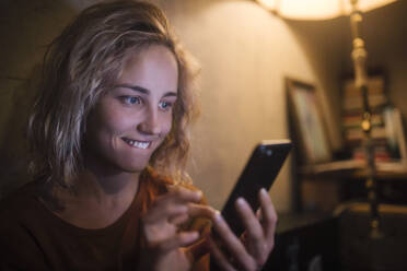 Portrait of young woman using smartphone at home - GCF00321