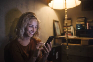 Porträt einer lächelnden jungen Frau, die zu Hause ein Smartphone benutzt - GCF00324