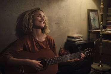 Happy young woman playing guitar at home - GCF00330