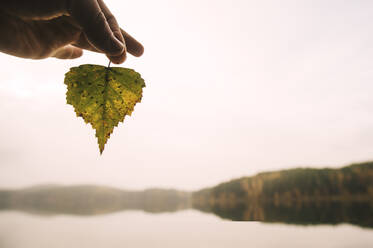 Hand hält Herbstblatt an abgelegenem See - BLEF10284