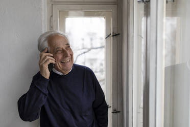 Happy senior man on cell phone at home - GUSF02037