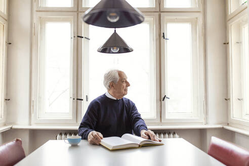 Älterer Mann liest Buch am Tisch zu Hause - GUSF02041