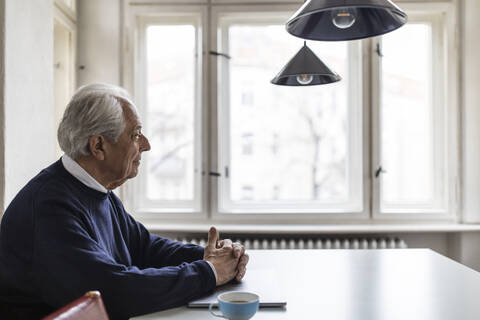 Älterer Mann sitzt am Tisch zu Hause, lizenzfreies Stockfoto