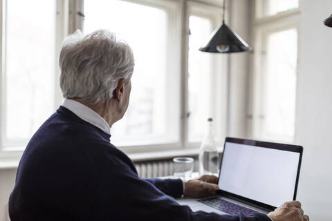 Älterer Mann benutzt Laptop auf dem Tisch zu Hause, lizenzfreies Stockfoto