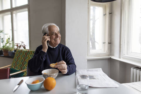 Lächelnder älterer Mann am Handy zu Hause, lizenzfreies Stockfoto