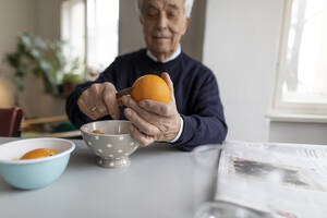 Älterer Mann schält zu Hause eine Orange - GUSF02053