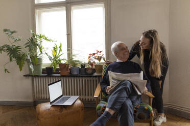 Glückliche junge Frau und älterer Mann mit Zeitung zu Hause - GUSF02057