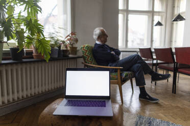 Älterer Mann zu Hause mit Laptop im Vordergrund - GUSF02060