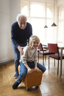 Happy grandfather and grandson playing with buck at home - GUSF02071