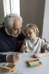 Watchmaker and his grandson examining watch together - GUSF02093