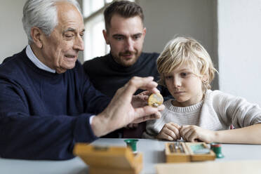 Watchmaker showing clockwork to young man and boy - GUSF02097