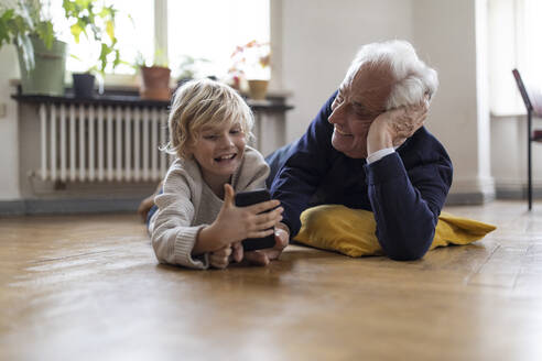 Großvater und Enkel liegen zu Hause auf dem Boden und benutzen ein Smartphone - GUSF02100