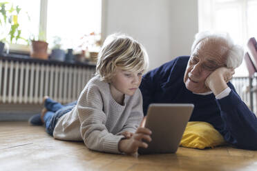 Großvater und Enkel liegen zu Hause auf dem Boden und benutzen ein Tablet - GUSF02101