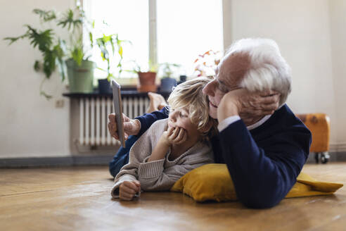 Großvater und Enkel liegen zu Hause auf dem Boden und benutzen ein Tablet - GUSF02102