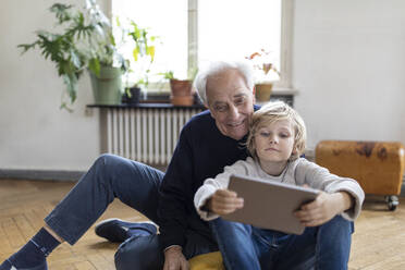 Großvater und Enkel sitzen zu Hause auf dem Boden und benutzen ein Tablet - GUSF02104