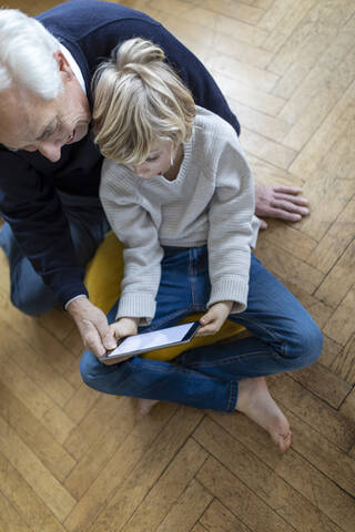 Grandfather and grandson sitting on the floor at home using a tablet stock photo