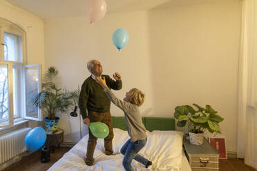 Glücklicher Großvater und Enkel spielen mit Luftballons auf dem Bett zu Hause - GUSF02127