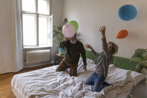 Happy grandfather and grandson playing with balloons on bed at home - GUSF02129