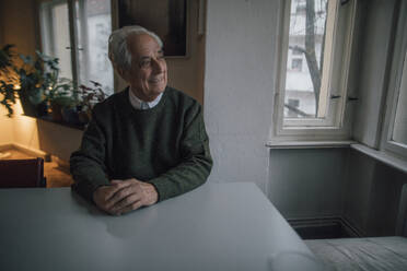Smiling senior man sitting at table at home - GUSF02133