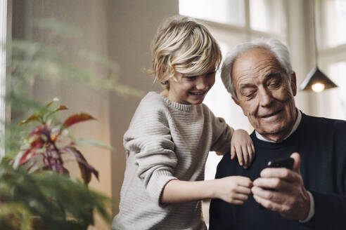 Happy grandfather and grandson using cell phone at home - GUSF02161