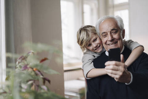 Glücklicher Großvater und Enkel telefonieren zu Hause mit dem Handy, lizenzfreies Stockfoto
