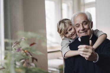 Happy grandfather and grandson using cell phone at home - GUSF02164