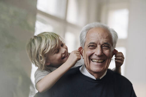 Happy grandson pulling grandfather's ears at home - GUSF02169