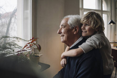 Happy grandson embracing grandfather at home - GUSF02172