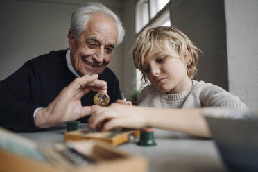 Watchmaker and his grandson examining watch together - GUSF02179
